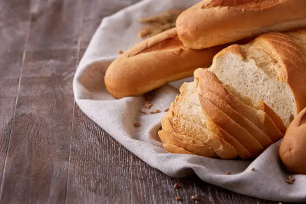 Slices of white bread and baguette laying on white cloth with gradient dark-brown background. Wooden table. With flour and wheat. Delicious. Tasty food.