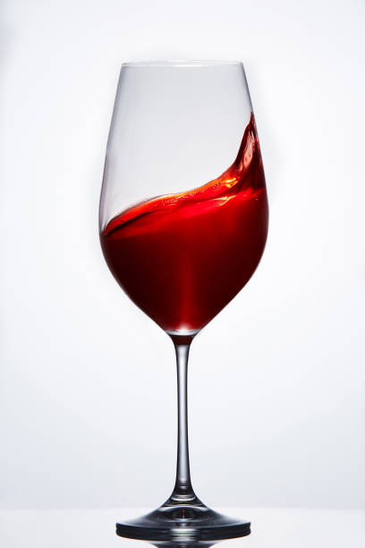 Elegant pure wineglass with wave of brightly red wine standing against light background with reflection in down. Elegant pure wineglass with wave of brightly red wine standing against light background with reflection in down. Relaxation and luxury lifestyle. Tasty and natural drink. Sommelier and tasting. Vertical photo. kachina doll stock pictures, royalty-free photos & images
