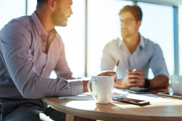 Business investors discussing business matters sitting at table in office. Business executives discussing work at office. Closeup of coffee cup with blurred image of two businessmen sitting on table. business meeting 2 people stock pictures, royalty-free photos & images