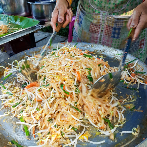 gotowanie słynnego tajskiego dania street food o nazwie "pad thai", które jest smażone danie z makaronem, kiełki fasoli, warzywa z kurczaka lub krewetki, zawinięte w cienki omlette. - obrotowa łopatka zdjęcia i obrazy z banku zdjęć