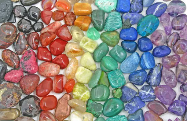 Background of red, orange, yellow, green, blue and purple colored tumbled crystal stone depicting the seven chakras