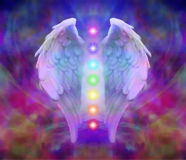 A pair of angel wings with the seven chakras between on a colorful ethereal energy background