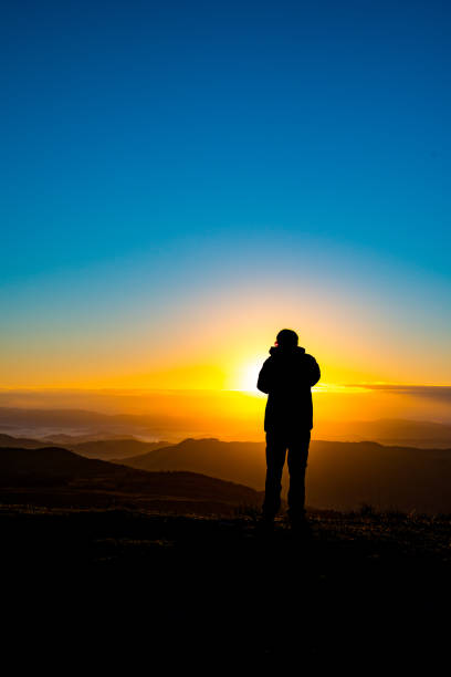 istock Photographer silhouette recording sunrise in mountains 689320648