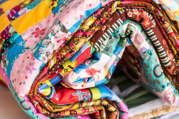 istock patchwork, sewing and fashion concept - macro of bright beautiful multi-colored quilt rolled up in the tube at shop, warehouse of finished stitched textile products, side view 689326990