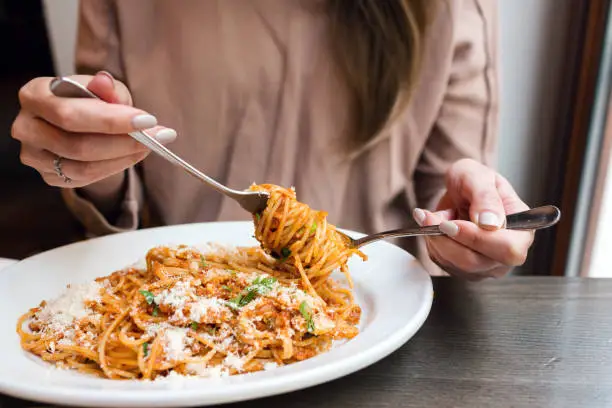 Photo of girl eats Italian pasta with tomato, meat. Close-up spaghetti Bolognese wind it around a fork with a spoon. Parmesan cheese