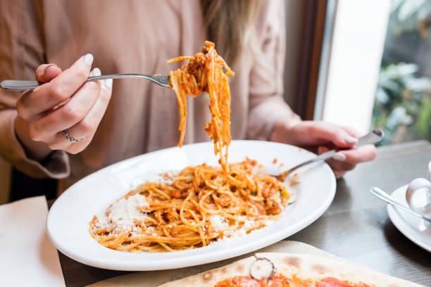 meisje eet italiaanse pasta met tomaat, vlees. close-up spaghetti bolognese wikkel het rond een vork met een lepel. parmezaanse kaas - spaghettibandjes stockfoto's en -beelden