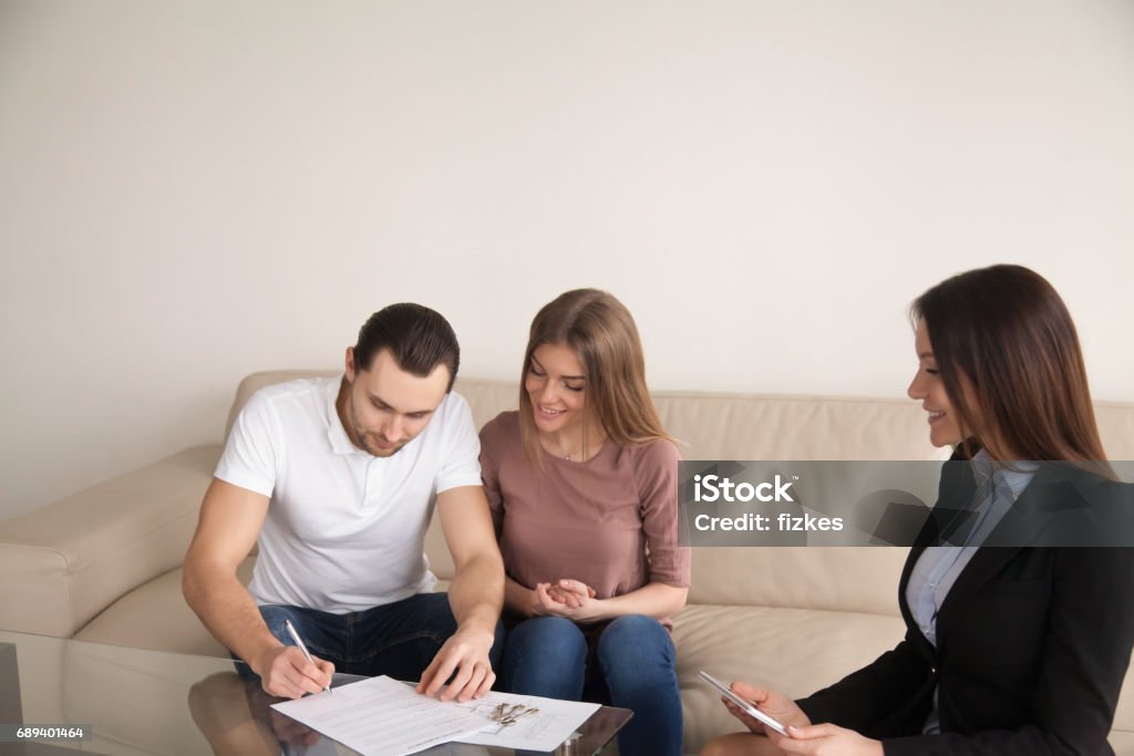 Couple signing agreement for buying renting apartment, mortgage or investment Couple meeting with female bank worker or real estate agent, signing loan agreement, mortgage contract, buying flat and getting keys of apartment, property investment, great purchase for young family Financial Loan Stock Photo
