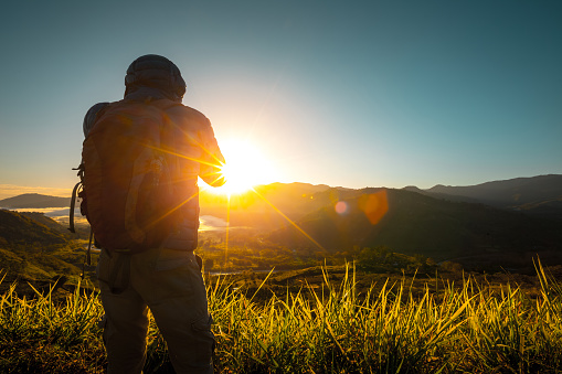 Hiker stands on the meadow with mountains on the background during sunrise