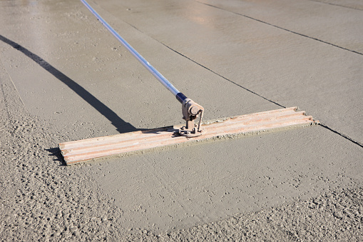 Bull float concrete finishing hand tool levels and smooths the surface of a cement slab foundation while settling the gravel mix within the cement below its surface.