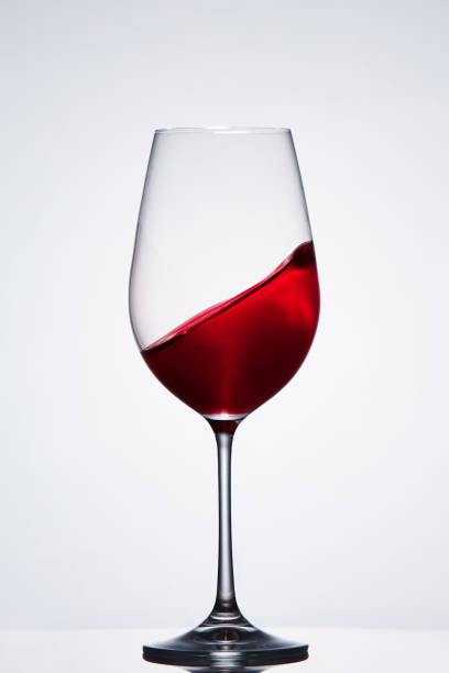istock Moving red wine in the pure fragile wineglass standing against light background with reflection. 689496944
