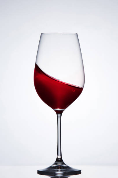 istock Moving red wine in the elegant wineglass standing against light background with reflection. 689496946