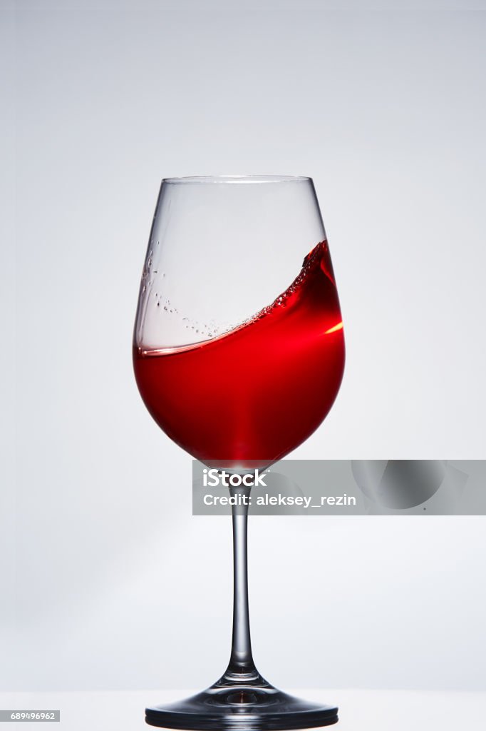 Elegant pure wineglass with wave of brightly red wine standing against light background with reflection in down. Elegant pure wineglass with wave of brightly red wine standing against light background with reflection in down. Relaxation and luxury lifestyle. Tasty and natural drink. Sommelier and tasting. Vertical photo. Alcohol - Drink Stock Photo