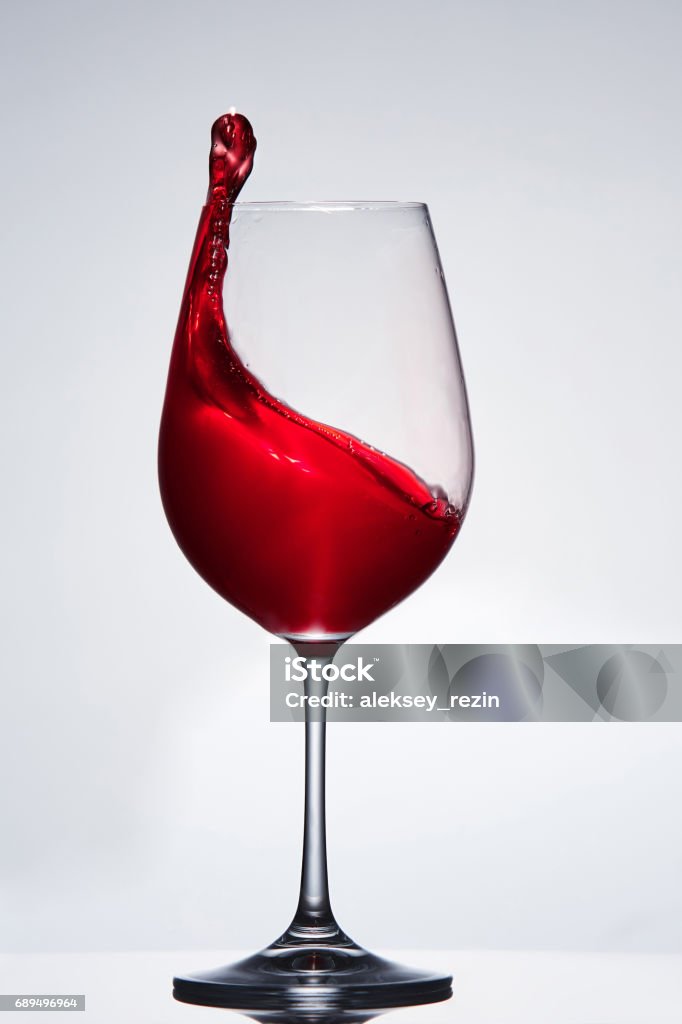 Elegant pure wineglass with wave of brightly red wine standing against light background with reflection in down. Elegant pure wineglass with wave of brightly red wine standing against light background with reflection in down. Relaxation and luxury lifestyle. Tasty and natural drink. Sommelier and tasting. Vertical photo. Alcohol - Drink Stock Photo