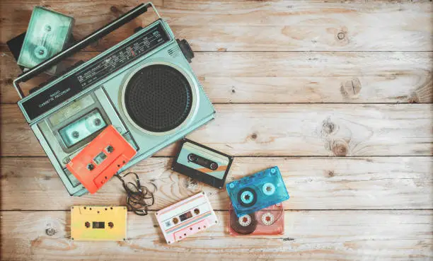 Top view hero header - retro technology of radio cassette recorder music with retro tape cassette on wood table. Vintage color effect styles.