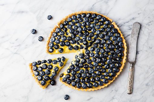 Blueberry tart with vanilla custard on a marble board. Top view. Copy space.