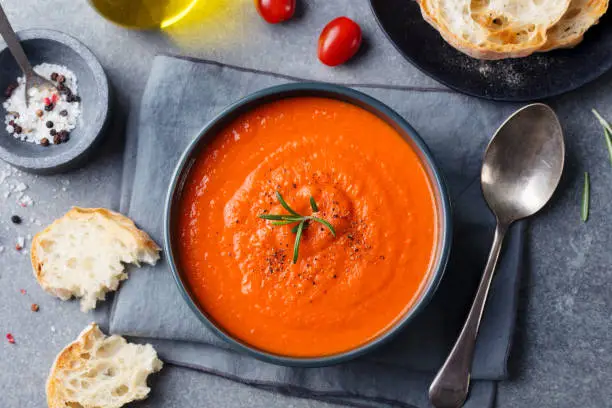 Photo of Tomato soup in a black bowl on grey stone background. Top view. Copy space.