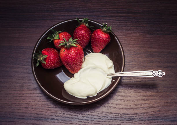 istock Strawberries with a spoon of cream on a plate 689550866
