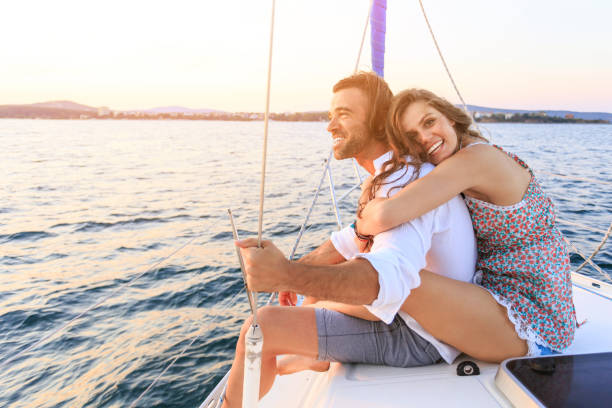Couple on honeymoon traveling with yacht Couple on honeymoon traveling with yacht. Woman sitting behind the man and hugging him. Both with casual clothes. caribbean beach sunset stock pictures, royalty-free photos & images
