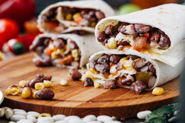 Nice vegetarian burrito over black table on wooden board.