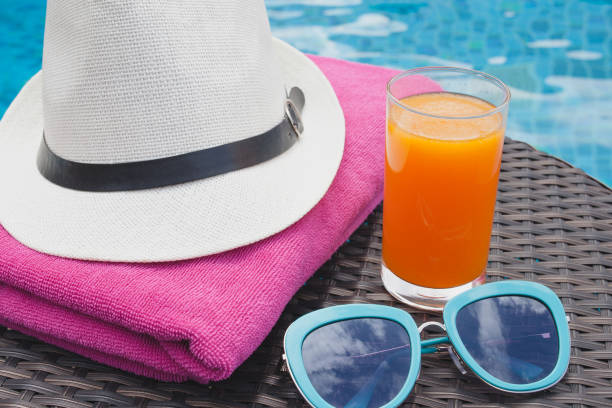 istock Summertime orange juice hat and sunglasses relax near swimming pool 689579708