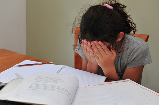 Young girl cries alone while sitting on the dining room table doing homework