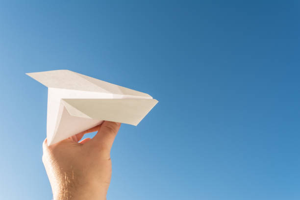 istock Hand holds white paper plane on blue sky 689630574