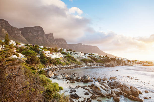 Beautiful sunset view of Table Mountain, the famous landmark in Cape Town, South Africa, with the setting sun glinting on windows in the distant city of Cape Town, at the mountain's foot. A dog's pawprints lead along the beach.