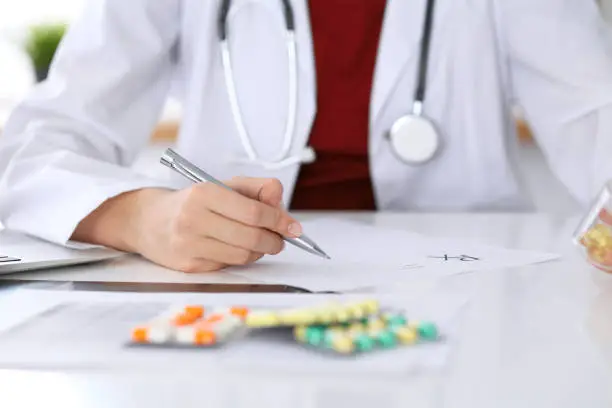 Female medicine doctor fills up prescription form to patient closeup. Panacea and life save, prescribe treatment, legal drug store, contraception concept.