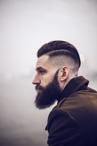 Profile view of young hipsterman with beard standing in the city