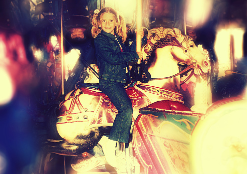 Vintage image of a girl riding a toy horse in a carrousel and looking at camera.