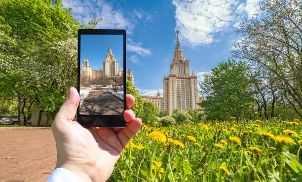 Photo of Conceptual view of large diversity of Moscow state university viewed through smart phone screen in human hand