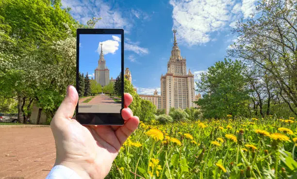 Photo of Conceptual view of large diversity of Moscow state university viewed through smart phone screen in human hand