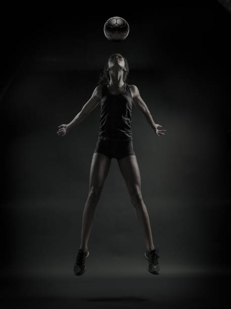 A desaturated image of an African Amercian women heading a soccer ball on a black background.