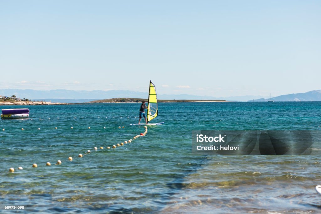 Windsurfing Young man learning windsurfing against clear blue sky.In distance people on the beach. Beach Stock Photo