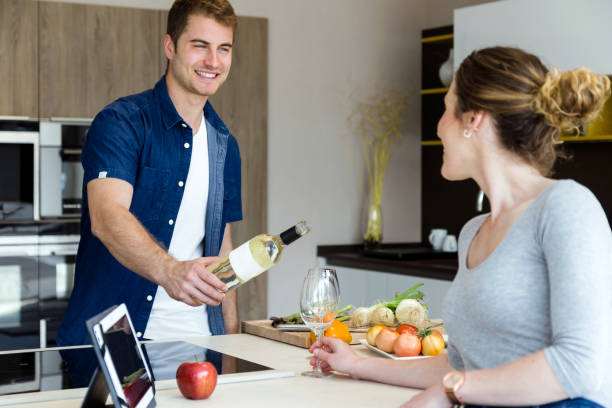 istock Handsome young man opening wine bottle while his wife using digital tablet in the kitchen. 689737488