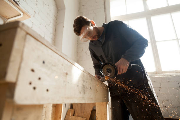 Man in protective glasses using angle grinder for cutting metal Worker in protective eyewear working in small workshop interior using die angle grinder for cutting steel bar, throwing sparks from metal grinding machine with abrasive disk wheel, making furniture grinding metal power work tool stock pictures, royalty-free photos & images