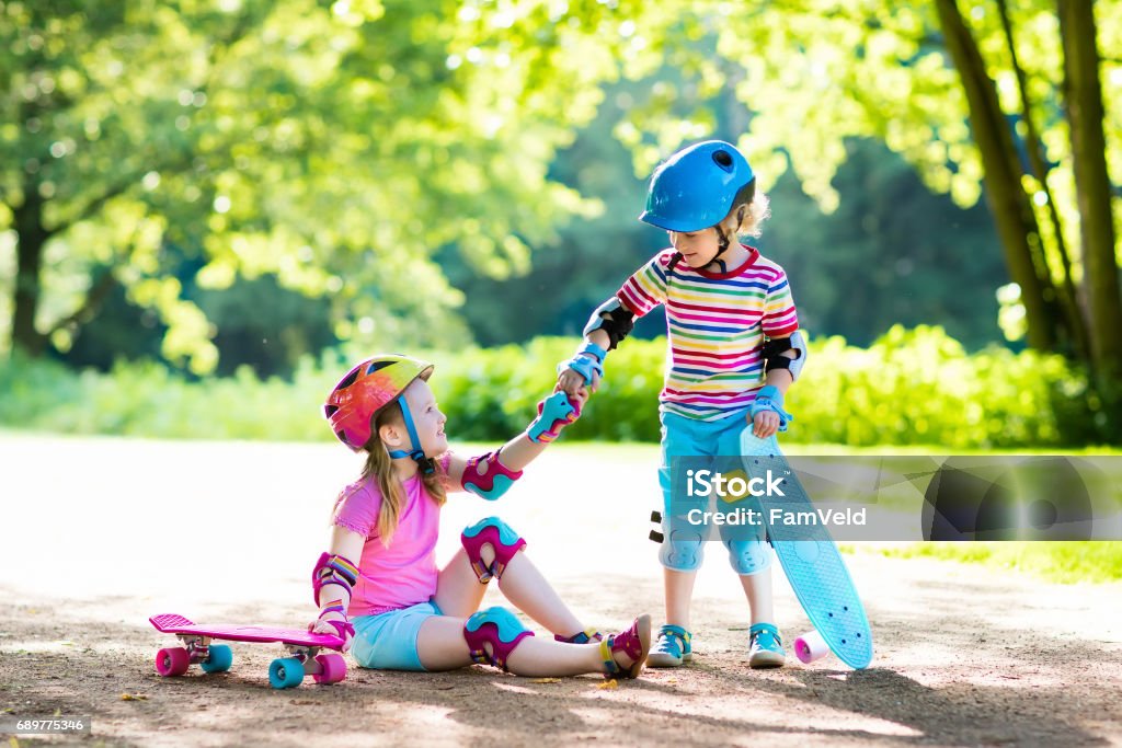 Children riding skateboard in summer park Children riding skateboard in summer park. Little girl and boy learn to ride skate board, help and support each other. Active outdoor sport for kids. Child skateboarding. Preschooler kid skating. Child Stock Photo