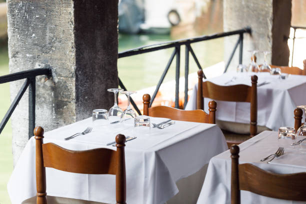 istock restaurant on the canal Venice. table setting for a lovey dinner. Empty glasses set in cafe. Part of interior. napkins, plates, and cutlery. 689781284