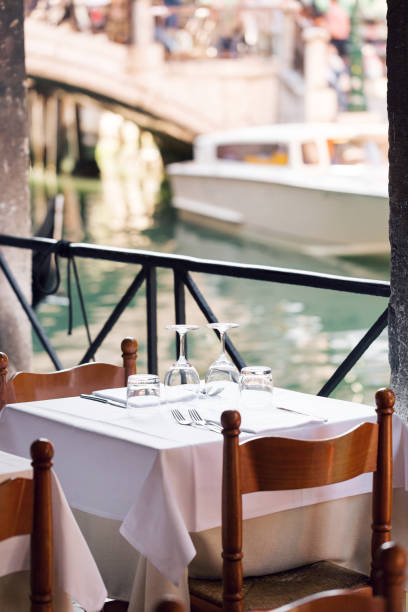 istock restaurant on the canal Venice. table setting for a lovey dinner. Empty glasses set in cafe. Part of interior. napkins, plates, and cutlery. 689781434