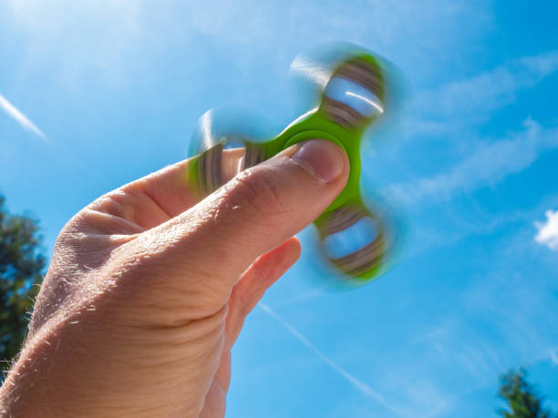 istock Male hand holding a fidget spinner against blue sky 689817966
