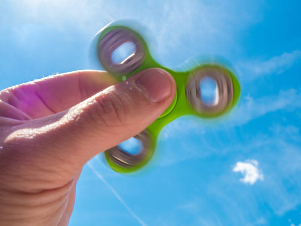istock Male hand holding a fidget spinner against blue sky 689818010
