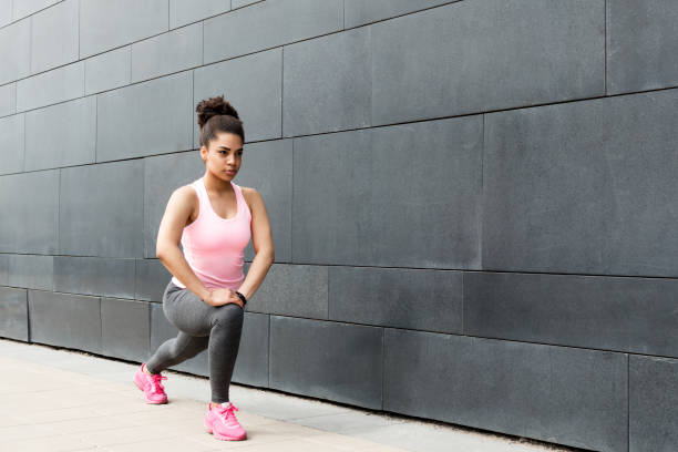 istock Young woman exercising outdoors, stretching leg at wall 689821544