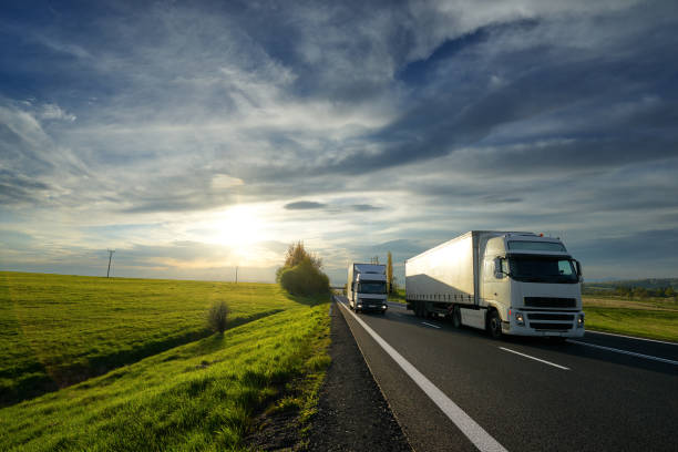 lkw überholt einen kleinlastwagen auf einer straße bei sonnenuntergang - diminishing perspective spring photography tree stock-fotos und bilder