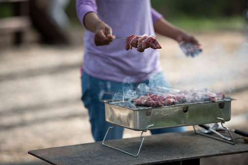 Close up unrecognized woman holding shashlik, preparing beef meat on a charcoal grill.