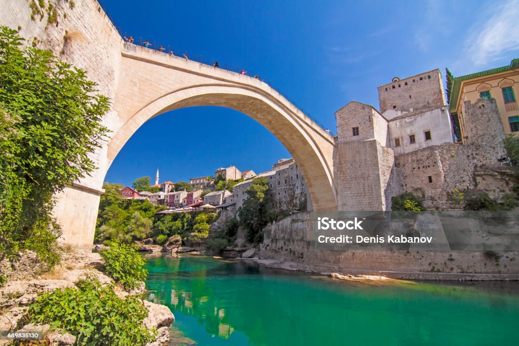 Old bridge over Neretva river in Mostar, Bosnia and Herzegovina Old Bridge (Stari Most), UNESCO World Heritage, and emerald river Neretva among rocks and old city buildings in summer sun lights. Mostar, Bosnia and Herzegovina Mostar Stock Photo