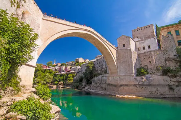 Old Bridge (Stari Most), UNESCO World Heritage, and emerald river Neretva among rocks and old city buildings in summer sun lights. Mostar, Bosnia and Herzegovina
