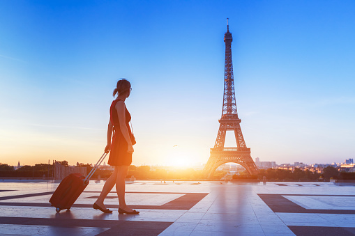 Silhouette of a woman tourist walking with a suitcase on Trocadero in front of Eiffel Tower, Paris, France