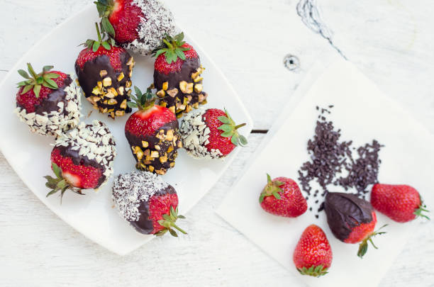 Strawberries covered with a chocolate Variety of strawberries covered with a dark chocolate with nuts pistachios and coconut on the white wooden table. Homemade choco dipped berry. Gourmet summer dessert. Top view. chocolate covered strawberries stock pictures, royalty-free photos & images
