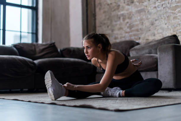 istock Slim sportswoman in sportswear warming-up muscles before workout doing stretching exercise sitting on floor at home 689890004