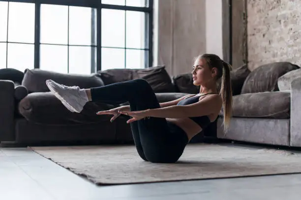 Photo of Slim sporty girl doing v-ups abs workout at home